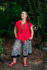 Storm Top - Red Apple Boho Top with cap sleeves and tie front, styled with colorful mandala culottes in a tropical garden setting.
